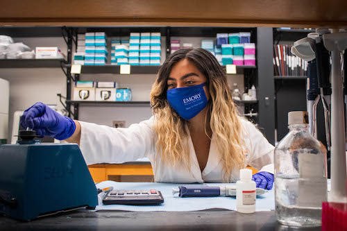 Student wearing a mask, at a desk using scientific tools